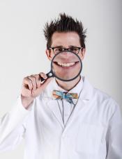 Alex Zerbe, also known as The Zaniac, wearing a lab coat and holding a magnifying glass