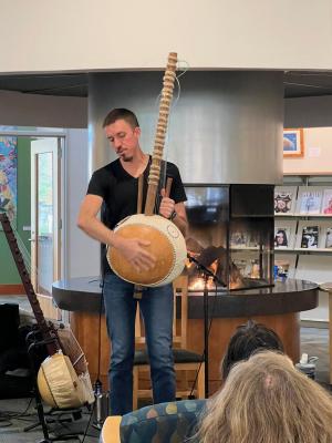 Photo of Sean Gaskell in front of hearth at Tualatin Library, Fall 2022, holding a kora, a 21-stringed West African harp.