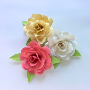Photo of 3 paper flowers in white, yellow, and pink, with green leaves, on a white background.