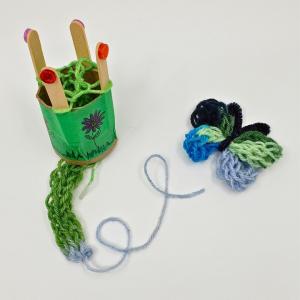 Photo of DIY knitting loom , holding green yarn, and a knit butterfly in shades of green and blue. 