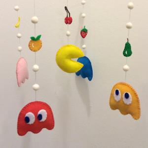 Photo of a mobile of Pacman characters and fruit in bright colors, hanging against a white wall.