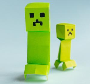 Photo of two Minecraft Creepers made from bright green paper on a pale blue background.