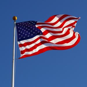 Photo of American flag, flying against blue sky.
