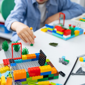 Photo of child in blurred background, behind a partially constructed LEGO™ object on a white desk.