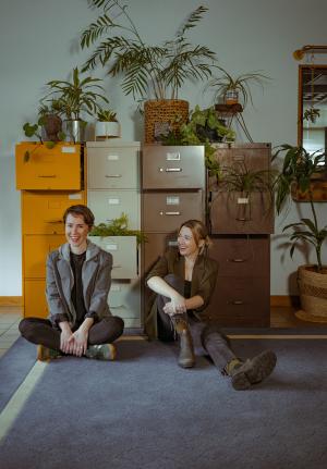 Danni Lee Parpan and Caroline Shaw seated on floor in front of filing cabinets. photo credit-Leah Vauter of Modspo.
