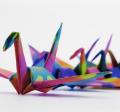 Photo of a row of origami paper cranes made with bright, colorful paper, on a white background.